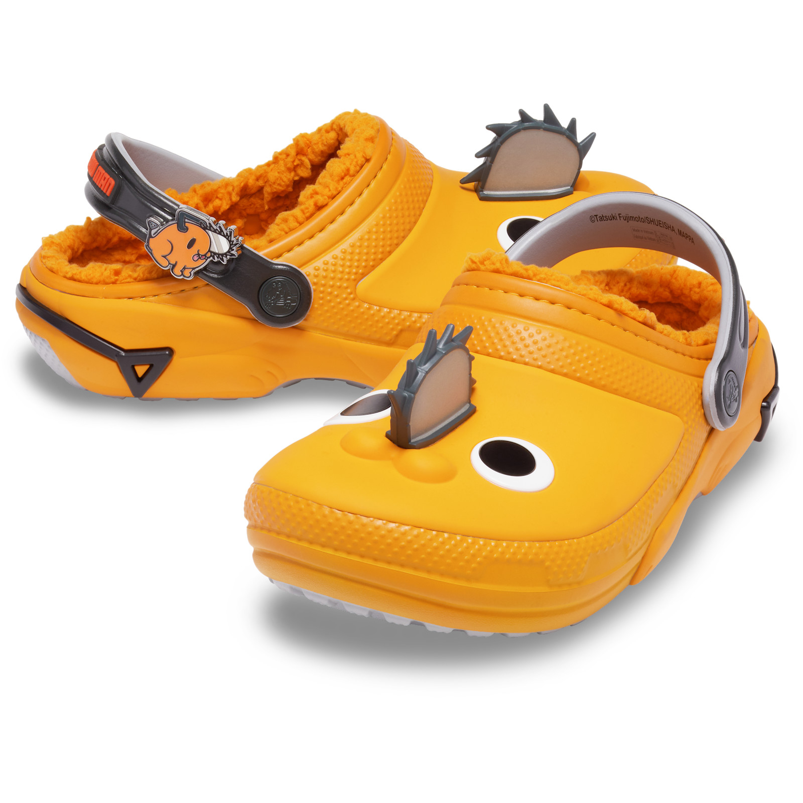 A pair of bright orange Crocs clogs designed as Pochita, with white eyes on the toes, a grey blade on the front, orange fuzzy lining and a black heel strap with a charm, on a white background.